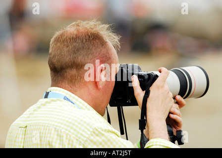 Un hombre fotógrafo con una cámara digital SLR con un lente de zoom telescópico lon tomando una fotografía adjunta foto Foto de stock