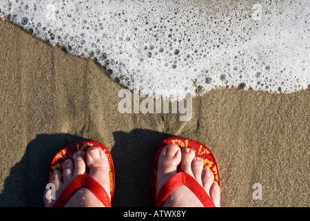 Dos pies vestidos de rojo flipflops stand en water's edge
