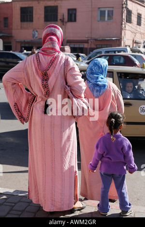 Dos mujeres con djellabas rosadas y una niña esperando junto a la carretera en el histórico barrio de Medina de Marrakech, Marruecos