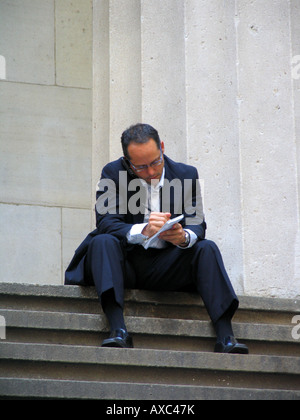 Hombre de negocios hablando por su teléfono celular y haciendo notas cerca de la Bolsa de Valores de Nueva York, EE.UU. en Wall Street, Manhattan, New Y Foto de stock
