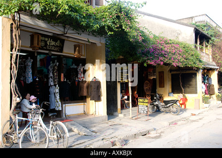 Escena callejera en Hoi An Vietnam mostrando una tienda de venta de ropa hecha de seda y una cafetería. Tranquila y segura. Cubiertas de árboles Foto de stock