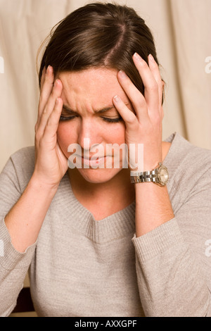 Mujer joven experimenta un dolor de cabeza, posiblemente una migraña. Foto de stock