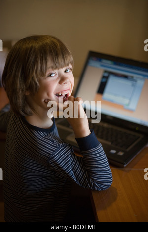 Niño de cinco años sonrisas para la cámara como él utiliza lap top computadora en casa Foto de stock