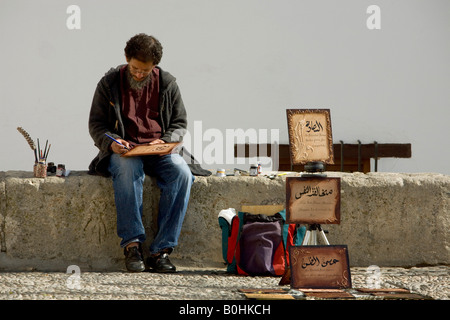 Venta de caligrafía árabe el hombre sentado en el Mirador de San Nicolás en el Albayzín o barrio de Albaicín de Granada, Andalucía, s