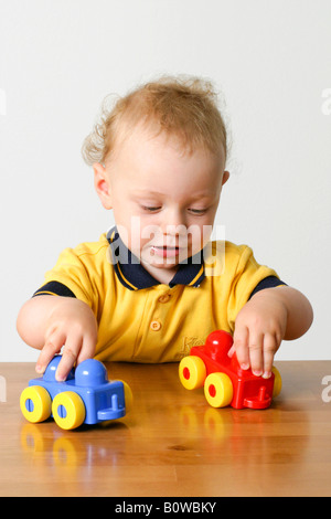 Uno-año-viejo muchacho jugando con dos coches de juguete