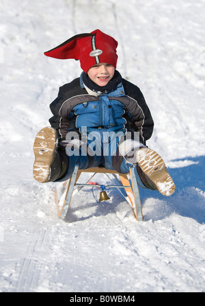 Cinco-año-viejo muchacho montar abajo de una colina en un trineo, trineo Foto de stock