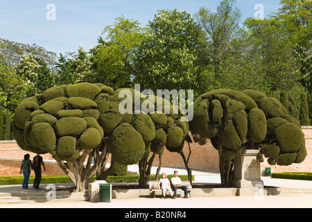 España Madrid gente sentada en un banco bajo los árboles en los jardines esculpidos en el Parque del Retiro el Parque del Buen Retiro. Foto de stock
