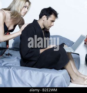 Hermosa joven pareja caucásica en una cama sobre el aislamiento del fondo con el ordenador portátil Foto de stock