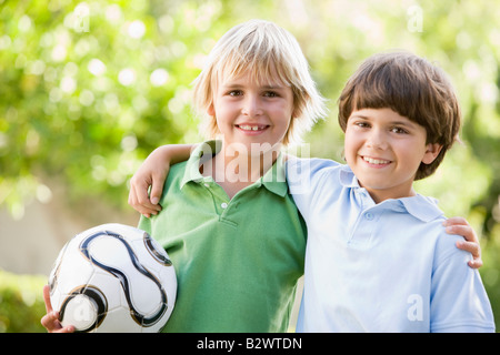 Dos chicos jóvenes al aire libre con una pelota de fútbol sonriendo