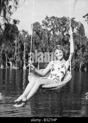 Retrato de una joven mujer sentada en un columpio en el lakeside y sonriente