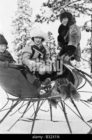 Mujer joven con sled vestida con ropa de invierno casual. Lindo gracioso  mestizos caucásicos mujer asiática sentado en el trineo retro cerca de nieve  cuesta abajo. Una mujer que padece en un