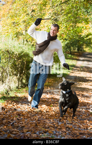 El hombre exterior con el perro en la ruta en el parque sucursal sonriendo (enfoque selectivo)