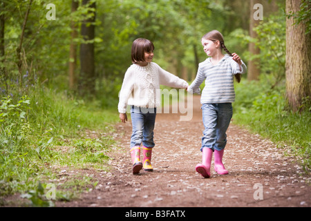 Dos hermanas caminando en el camino tomados de la mano sonriendo Foto de stock