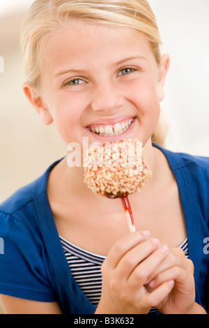 Niña adentro comiendo caramelos sonrientes de apple Foto de stock
