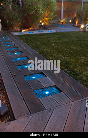 Decking camino iluminado por luces de cristal azul en el jardín moderno