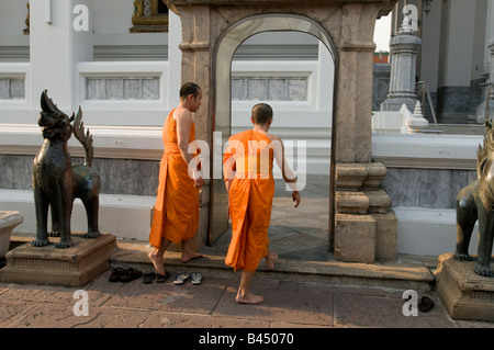 Dos monjes se deshacen de sus zapatos y entran en el edificio que alberga el enorme Buda reclinado en Wat Pho Bangkok Tailandia Foto de stock
