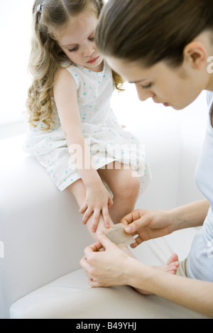 Madre poniendo venda adhesiva sobre la joven hija de la pierna Foto de stock
