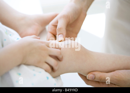 Adulto colocando vendaje adhesivo en la rodilla del niño, vista recortada Foto de stock