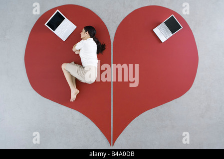Mujer tendida en el suelo con un portátil de gran corazón roto, abandonado detrás de su portátil Foto de stock
