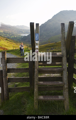 Mujer caminando hasta la escalerilla stile en cabeza del valle mirando hacia abajo a lo largo de Llyn Gwynant, Snowdonia, Gales