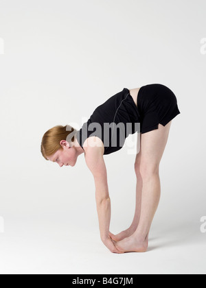 Una joven mujer que practica el 'ascendente' yoga pose plegado hacia adelante Foto de stock