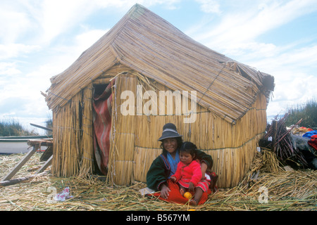 Muchacha nativa y su hermana pequeña sentado junto a una choza hecha de Reed en un uro Isla cerca de Puno Foto de stock