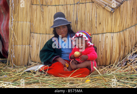 Muchacha nativa y su hermana pequeña sentado junto a una choza hecha de Reed en un uro Isla cerca de Puno Foto de stock