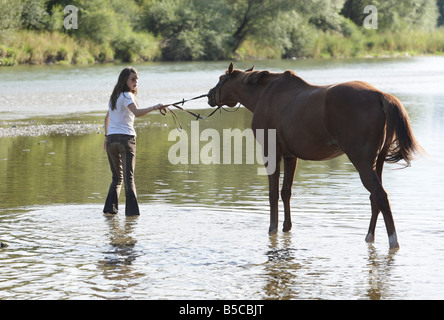 Adolescente paseos a caballo a través de un río superficial