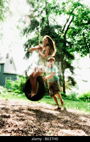 Adolescente balanceándose en un columpio de neumático con un joven empujándola Foto de stock