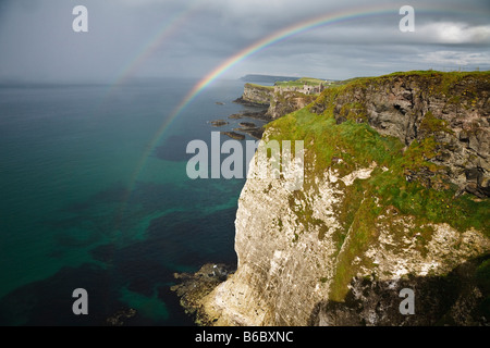 Un doble arco iris sobre los acantilados de rocas blancas y vista hacia el Castillo de Dunluce en la costa del norte de Antrim, Irlanda del Norte