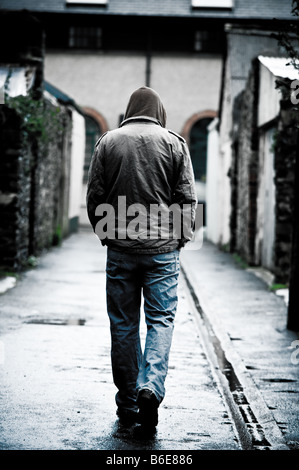 Joven llevaba una chaqueta con capucha solos y aislados, caminando por un callejón en una ciudad UK visto desde atrás caminando
