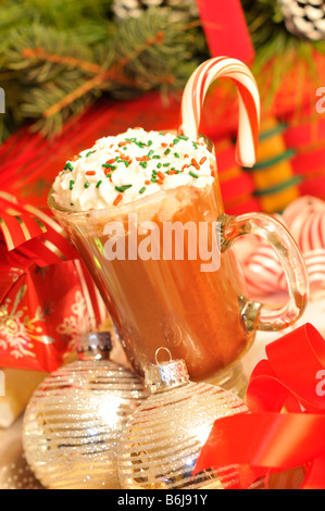 Holiday chocolate caliente con crema batida y espolvorea y regalos en la mesa delante del árbol Foto de stock