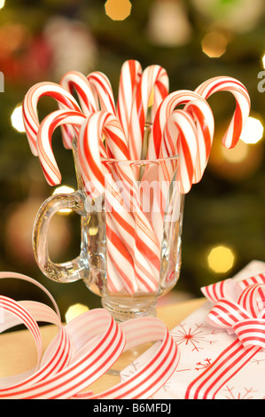 Vaso de bastones de caramelo con cinta actual y la iluminación del árbol de navidad en segundo plano. Foto de stock