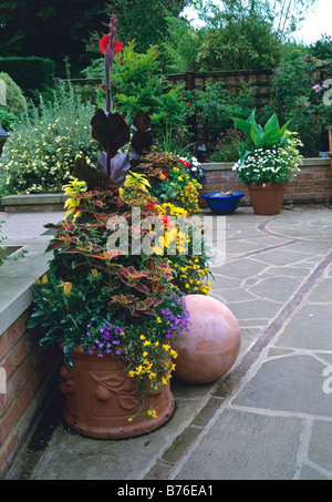 Bola de terracota y contenedores plantados en colores calientes sobre una terraza de piedra Foto de stock