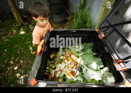 Muchacho de seis años mira en compost bin en el jardín Foto de stock