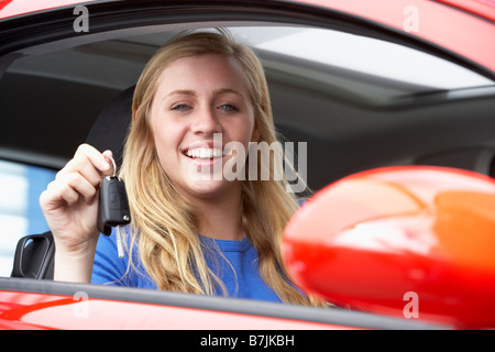Adolescente sentado en el coche, sosteniendo las llaves del coche y sonriendo a la cámara Foto de stock