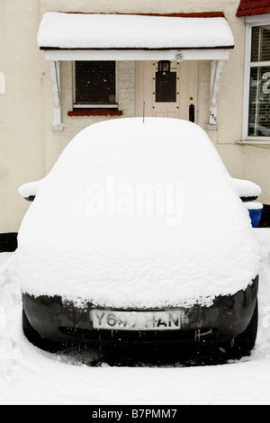 Cubierto de nieve un coche aparcado delante de una casa Foto de stock
