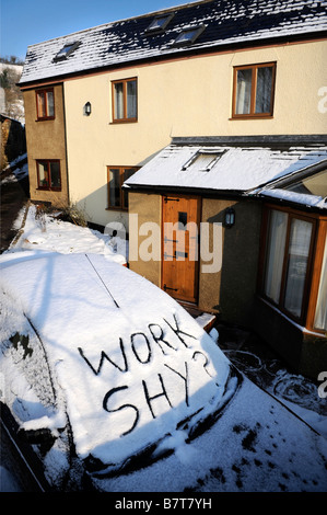 Coche aparcado en un camino con palabras trabajo tímido escrito en la nieve sugiriendo el absentismo laboral durante condiciones invernal moderada Foto de stock