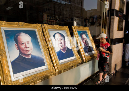 Un joven contempla retratos, los líderes de China mientras su madre tiendas gangas un almacén adyacente, Beijing, China Foto de stock