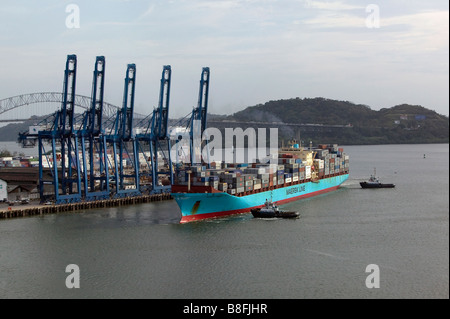 Vista aérea por encima de las grúas de Puerto Balboa Panamá remolcadores escolta buque contenedor cargado hacia el canal de Panamá Foto de stock