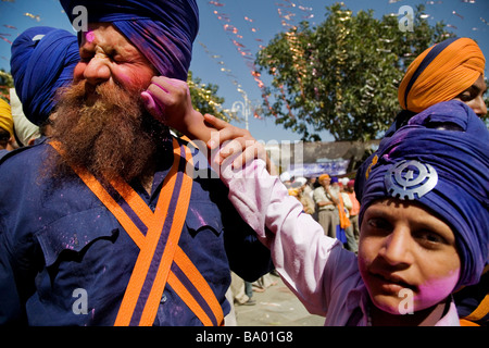 Un joven Nihang/Akali/sij, aplica el color en el rostro de su padre durante el festival de Holla Mohalla en Anandpur Saheb, Punjab, India Foto de stock