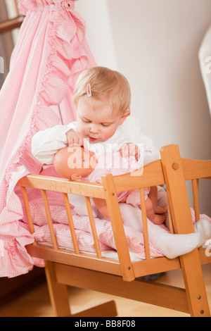Niña de 1 año de edad, sentada en su cochecito de muñeca y jugar con una muñeca Foto de stock