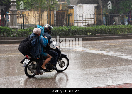 3 personas montando scooter en carretera mojada en Heavy Rain, 'Ninh Binh, Vietnam, [el Sudeste Asiático] Foto de stock
