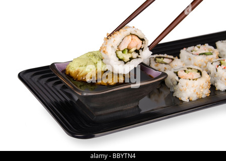 Un sushi fresco rollo de cangrejo y el pescado se sumerge en salsa de soja y wasabi usando palillos chinos y una elegante bandeja de servir Foto de stock