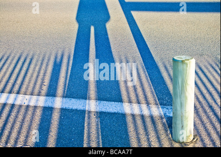 Largas sombras de un par de piernas y valla sobre asfalto Foto de stock