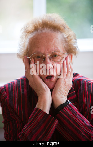 Una anciana se sienta cuidadosamente en la ventana Foto de stock
