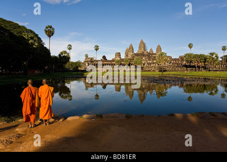 Vista clásica de Angkor Wat a través de las piscinas con un reflejo claro, con dos monjes túnicas naranja en primer plano Foto de stock