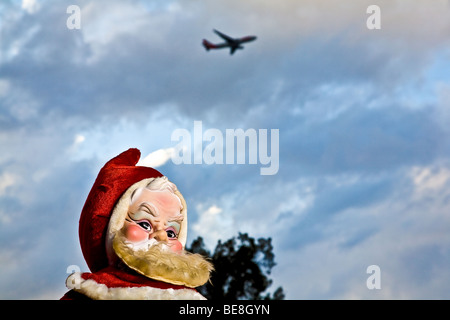Un peluche era de 1960 Santa Claus se encuentra en la luz del atardecer como un avión vuela por sobrecarga Foto de stock