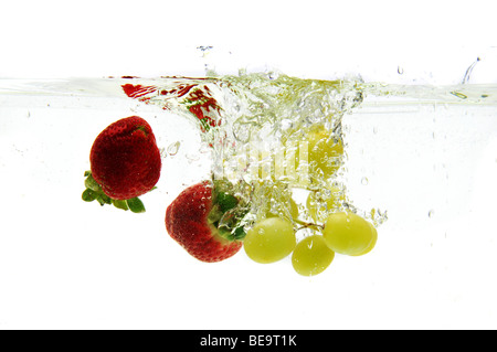 Las fresas y uvas cae al agua aislados sobre un fondo blanco.