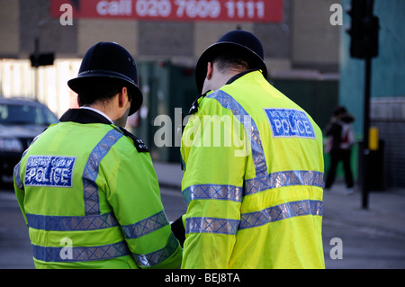 Dos funcionarios de la Policía Metropolitana en amarillo chalecos reflectantes visto desde atrás Foto de stock